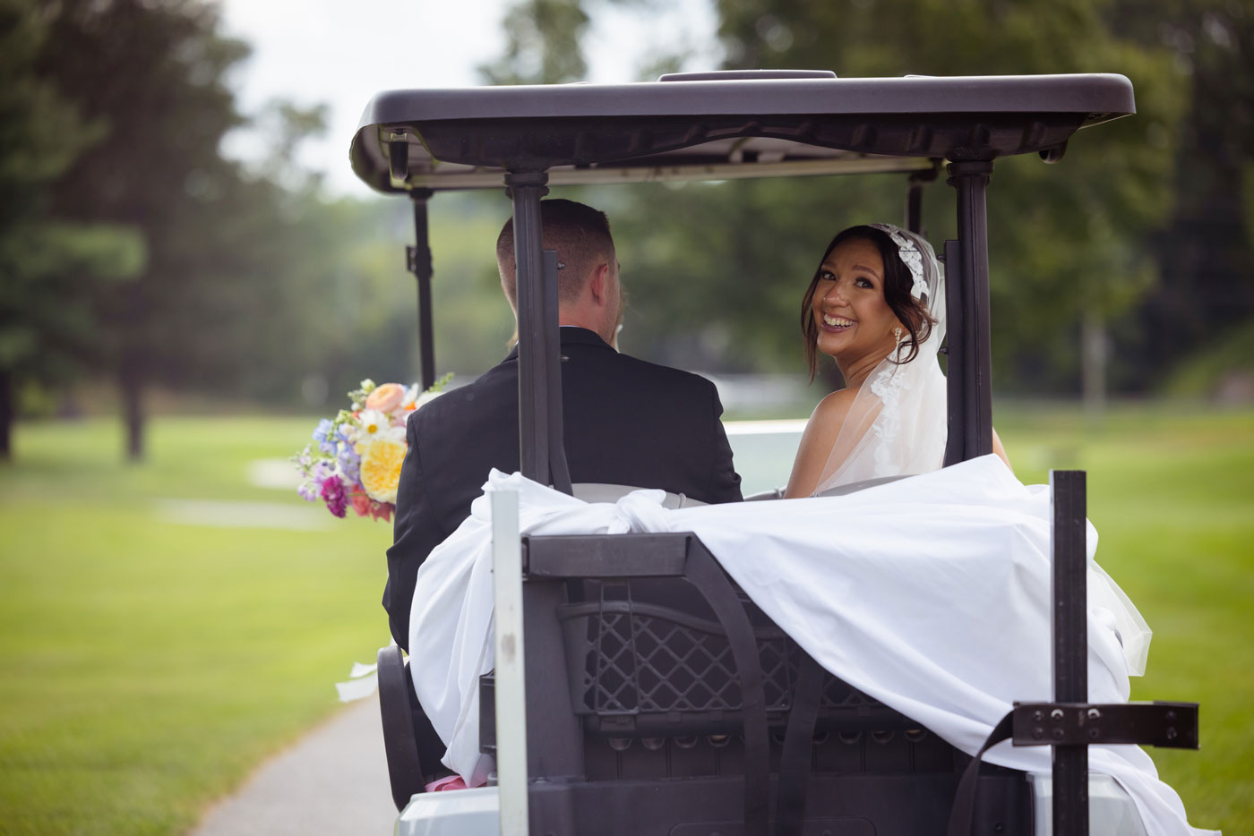 Bride and groom riding in a golf cart after their West Hills Country Club wedding