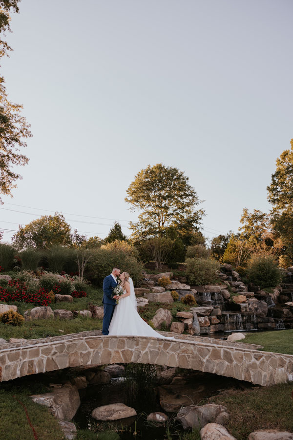 Couple standing near gardens and waterfall at sunset at West Hills Country Club